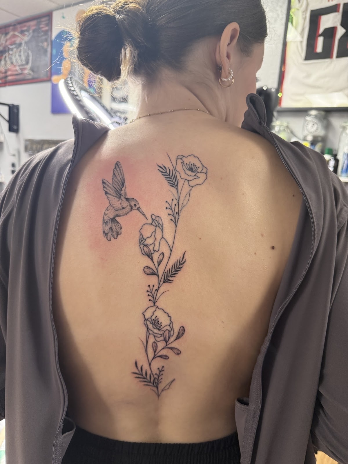 Fine line hummingbird and poppies running down a customer's spine