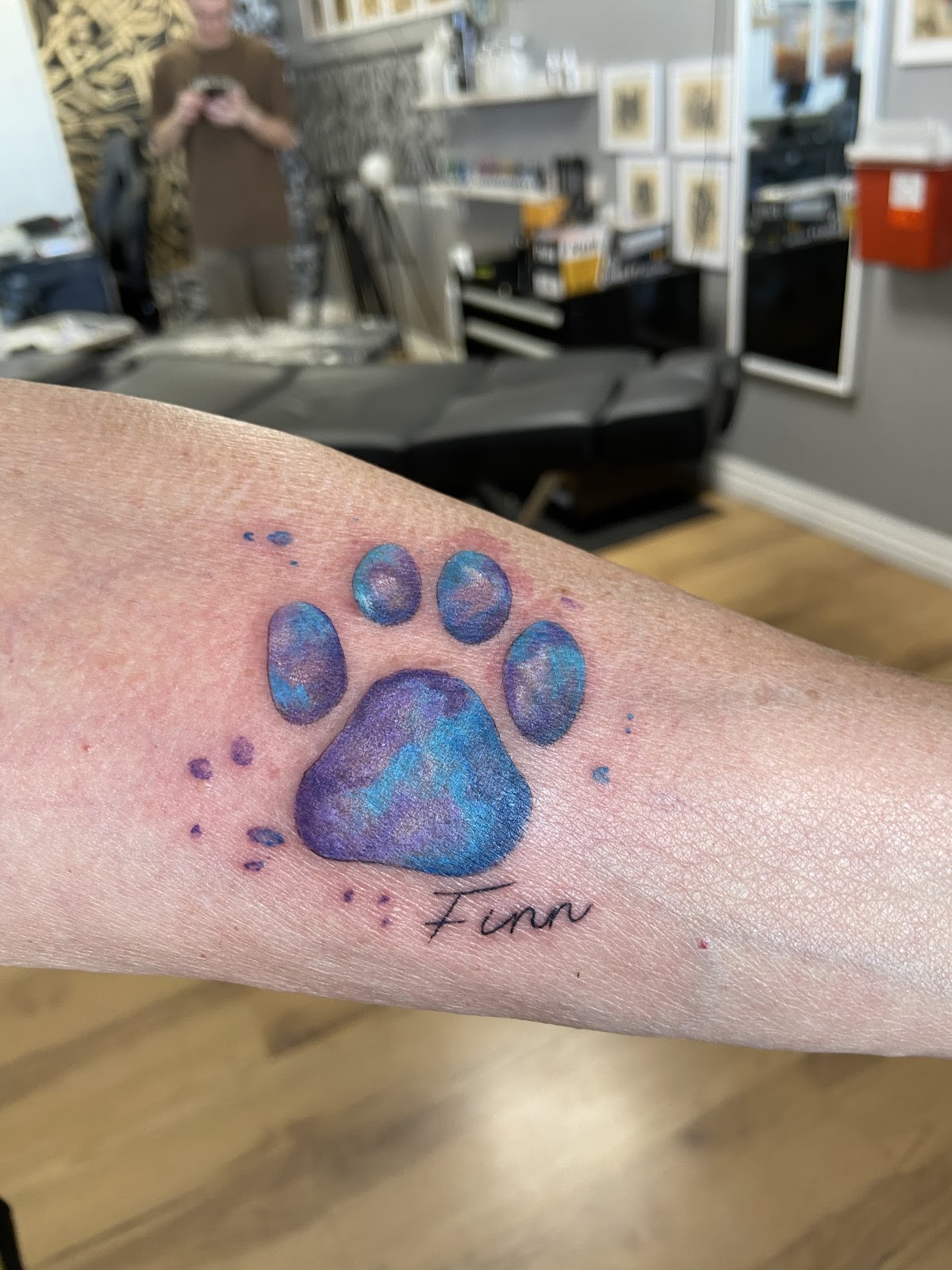 Watercolor paw print in blues and purples with the name Finn, on a forearm