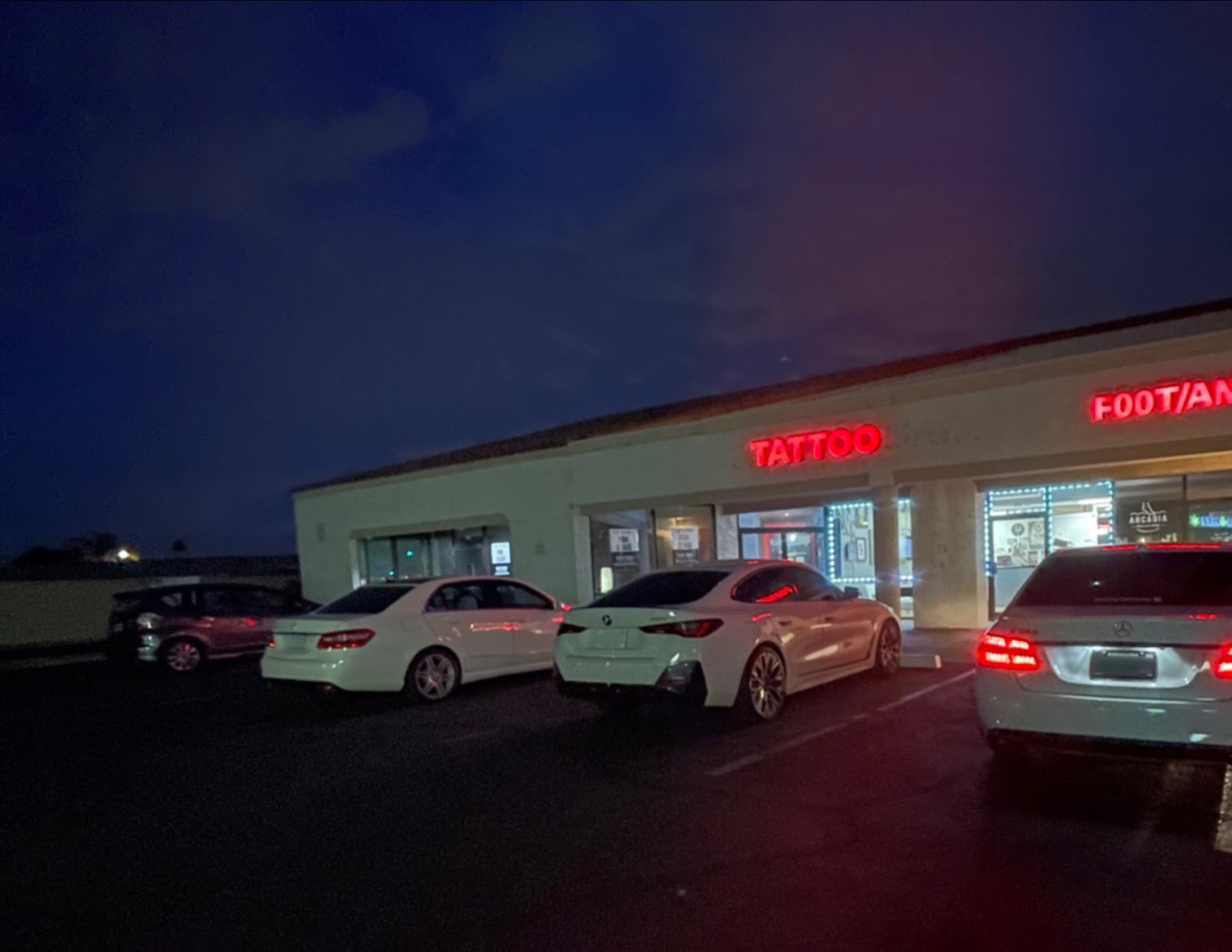 The red TATTOO sign glowing above the shop at night in the Bell Road plaza