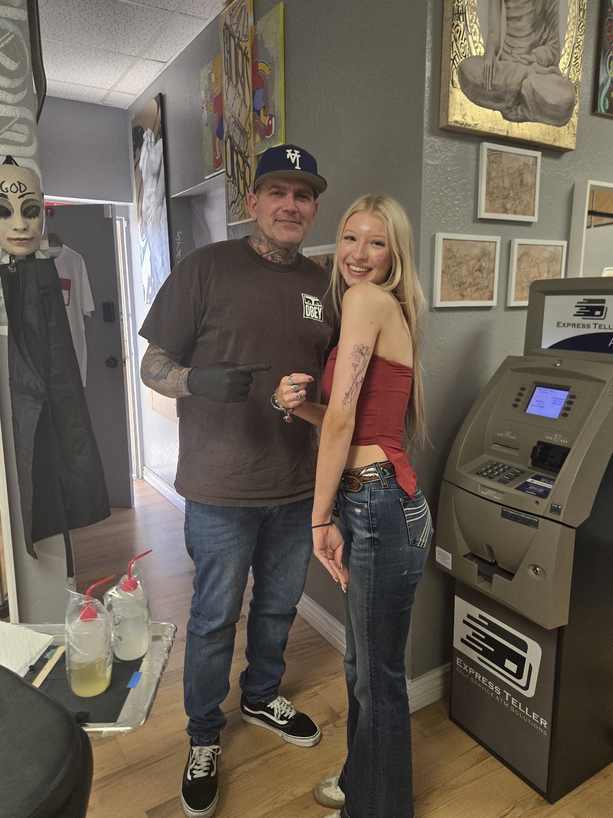Smiles at the front counter after a finished tattoo, with the in-shop ATM in the corner