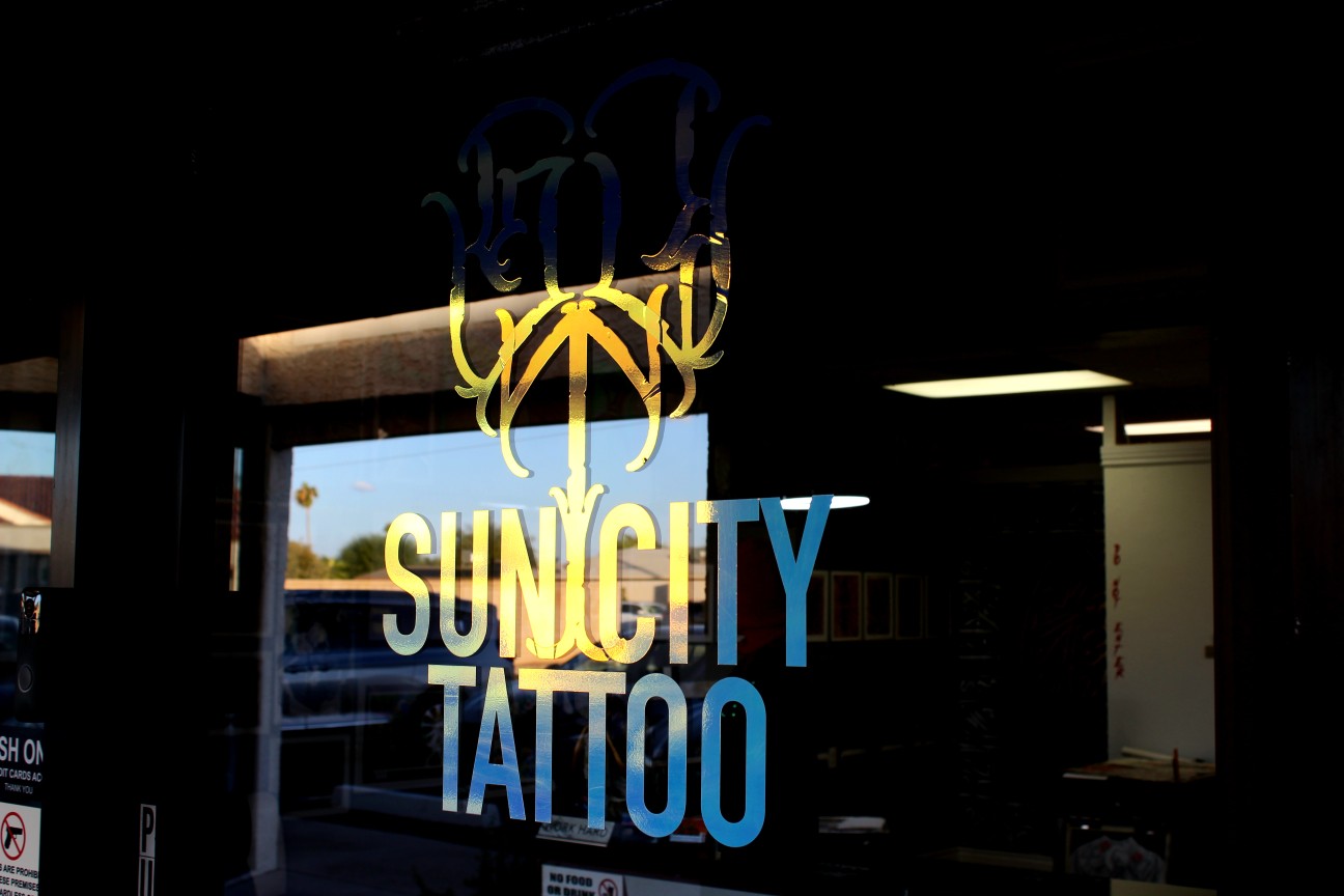 Sun City Tattoo lettering and ornate monogram on the front window, catching gold and blue afternoon light