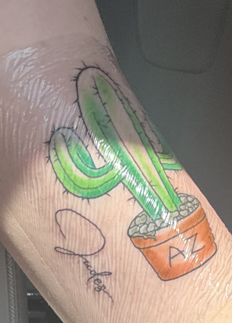 Color tattoo of a saguaro cactus in an orange pot labeled AZ, with a script signature