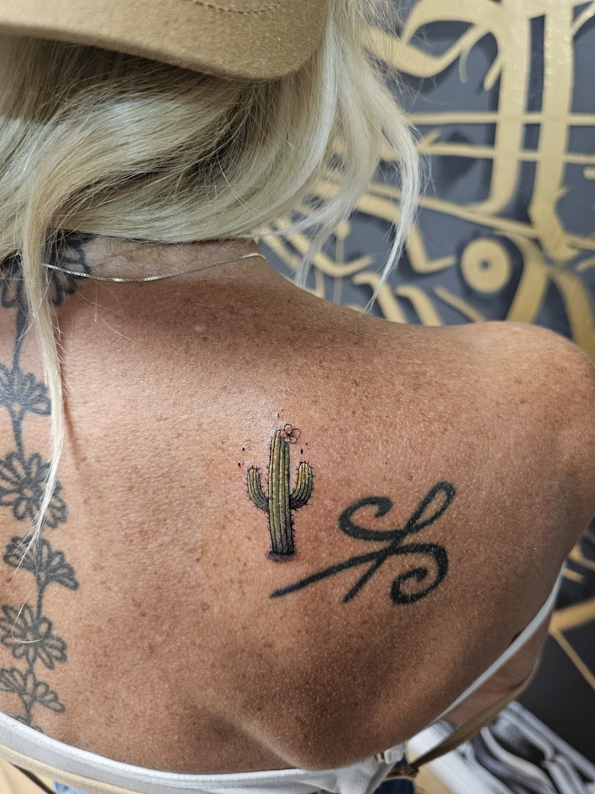 Small color saguaro cactus with a pink bloom on a shoulder, gold calligraphy mural behind